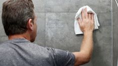 a man wiping his hands with a towel on the shower wall next to a shower head