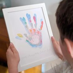 a young boy holding up a framed hand print