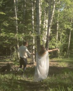 a man and woman are walking through the woods in front of some tall birch trees