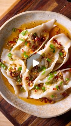 dumplings with sauce and green onions in a white bowl on a wooden cutting board