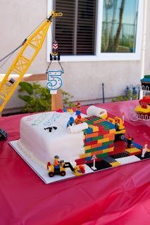 a birthday cake with legos on it and a crane in the background that says, ok, who wants to make this for me?