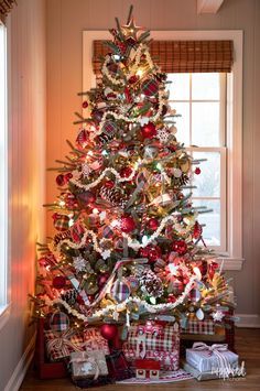 a christmas tree with presents under it in front of a window, decorated for the holiday season