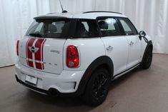 a small white car with red stripes parked in a room next to a curtained wall