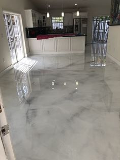 an empty room with shiny floors and white cabinets in the backround, leading to a large kitchen