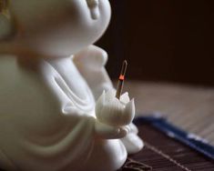 a small white buddha statue sitting on top of a wooden table next to a needle