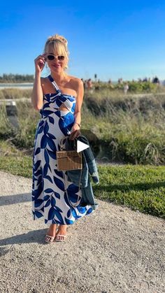 a woman in a blue and white dress is standing on a dirt road with her purse