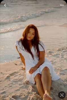 a woman is sitting on the beach with her feet in the sand and looking at the camera