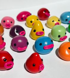 there are many different colored plastic toys in the shape of ducks and fish faces on this white surface