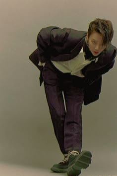 a man in a suit and sneakers is doing a trick on a skateboard against a gray background