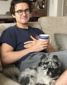 a man sitting on a couch holding a coffee cup with his dog laying next to him