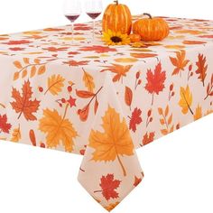 an orange and white table cloth with fall leaves on it, next to two wine glasses