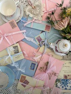 many different types of cards and papers on a table with teacups, saucers, and flowers