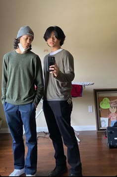 two young men standing next to each other in a room with hard wood flooring