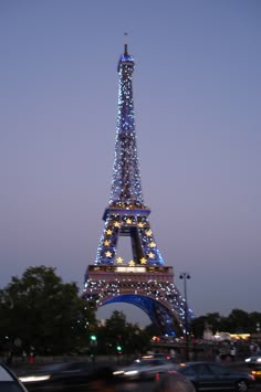 the eiffel tower lit up at night with cars passing by in front of it