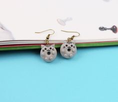 a pair of white cat earrings sitting on top of a blue table next to a book