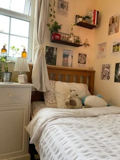 a bed with white sheets and pillows in a bedroom next to a window filled with plants