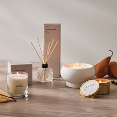 an assortment of candles, reeds and boxes on a wooden table with greenery