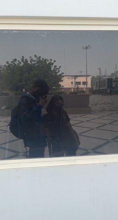 two people standing in front of a window looking at their cell phones and taking pictures