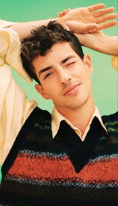 a young man with his hands on his head wearing a sweater and looking at the camera