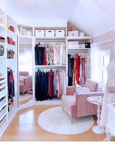 an organized closet with clothes on hangers, and a pink chair in the corner