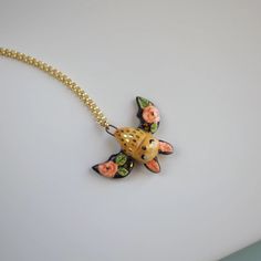 a gold necklace with an orange and black cat on it's back, sitting on a white surface