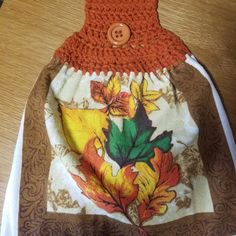 an orange crocheted bag with leaves on it sitting on a wooden table next to a button