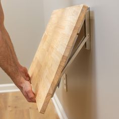 a person holding a piece of wood in their hand near a wall mounted shelf on the wall