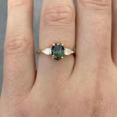 a woman's hand with a green and white diamond ring on top of it