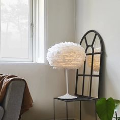 a white lamp sitting on top of a table next to a mirror and chair in a room