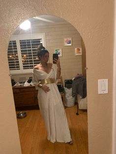 a woman taking a selfie in a mirror wearing a white dress and gold belt