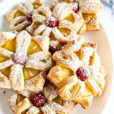 several small pastries on a white plate with powdered sugar and raspberries