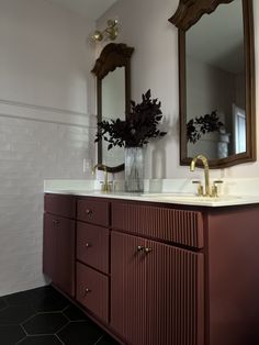 a bathroom vanity with two mirrors above it and a vase filled with flowers on the counter