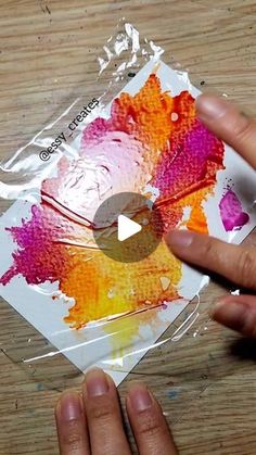 someone is painting with acrylic paint on a piece of paper that has been wrapped in plastic