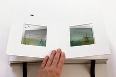 a hand is holding an open book with two pictures on the pages and one in the middle