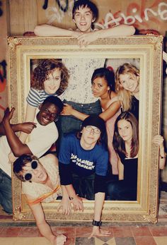 a group of young people posing in front of a framed photo with graffiti on the wall behind them