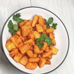 a white bowl filled with cooked carrots and cilantro on top of a wooden table