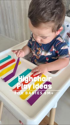 a little boy that is sitting in a highchair playing with some colored sticks