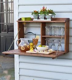 a wooden shelf with drinks and glasses on top of it, hanging from the side of a house