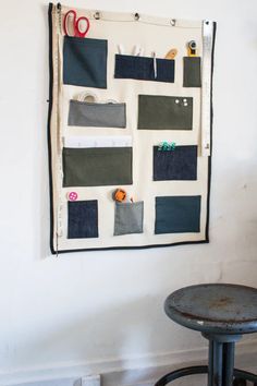 a piece of fabric hanging on the wall next to a stool with scissors and tape