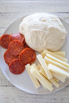 a white plate topped with cheese, pepperoni and sliced up sausage next to a baguette