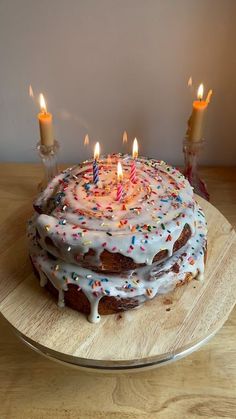 a birthday cake with white frosting and lit candles on a wooden platter,