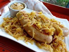 a white plate topped with two hot dogs covered in sauerkraut next to a bowl of mustard