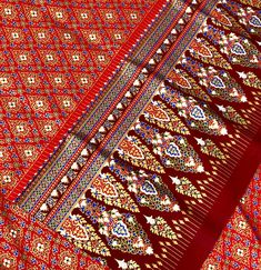 an intricately designed red cloth with gold and blue designs on the edges is shown in close up