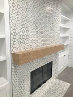 a fireplace in a room with white and gray tiles on the wall, shelves behind it