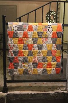 an orange and gray quilt hanging from a black iron railing in front of a house