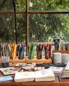 the desk is full of books, pens and pencils in front of an open window