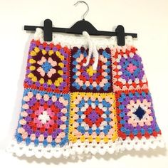 a colorful crocheted skirt hanging on a clothes hanger with two black hooks