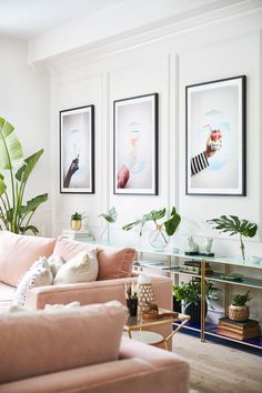 a living room with pink couches and pictures on the wall above them, along with plants in vases