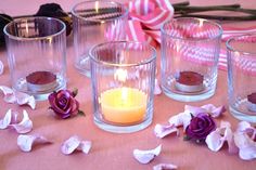 candles and flowers sit on a table with pink ribbon in the background, along with other glass vases