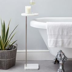 a white bath tub sitting next to a potted plant and a candle on a stand